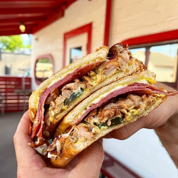 A hand holds a large, sliced Italian sandwich filled with meats, cheese, and mustard.