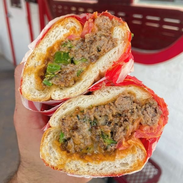 A hand holds a halved Italian meatball sub sandwich with red and white striped paper.