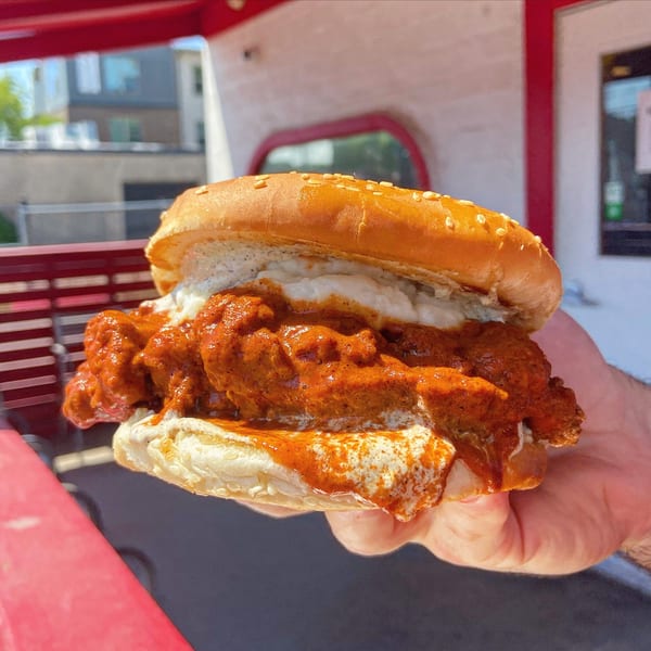 Hand holding a Picone Italian meatball sandwich with red sauce and white cheese on a sesame bun.